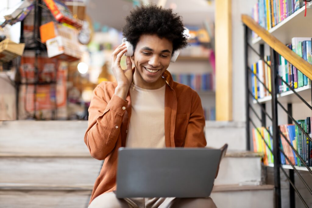 Ung mann med hodetelefoner og pc i bibliotek