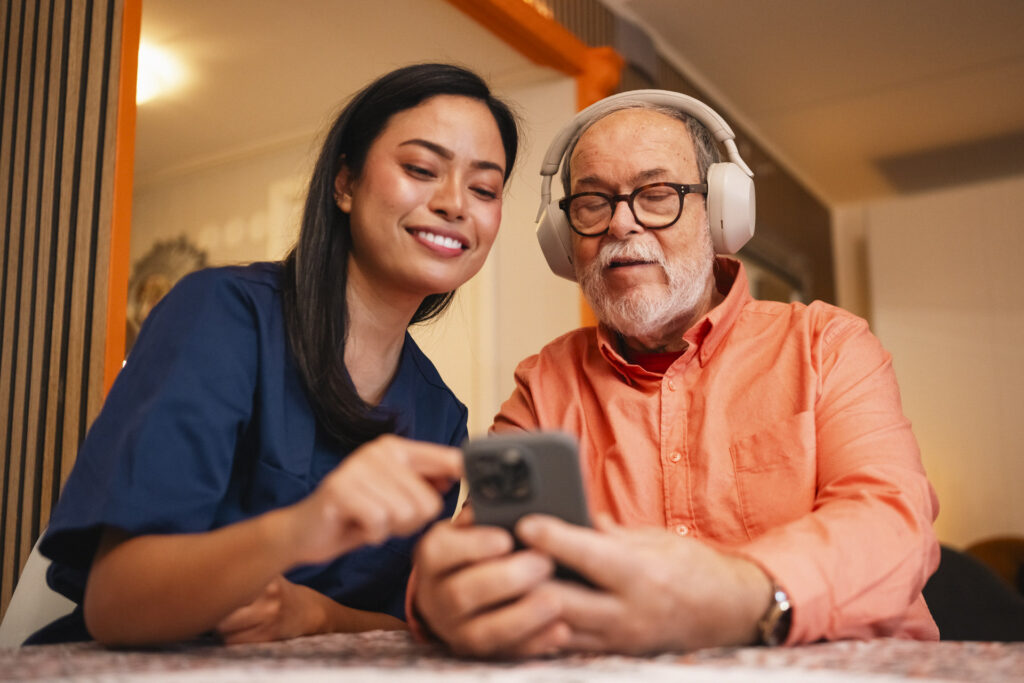 Eldre låner med hodetelefoner ser på mobilen sammen med en helsearbeider