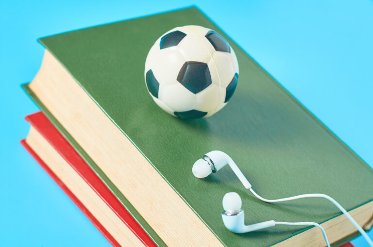 En liten fotball og et par høretelefoner plassert på toppen av en bunke bøker. Foto.