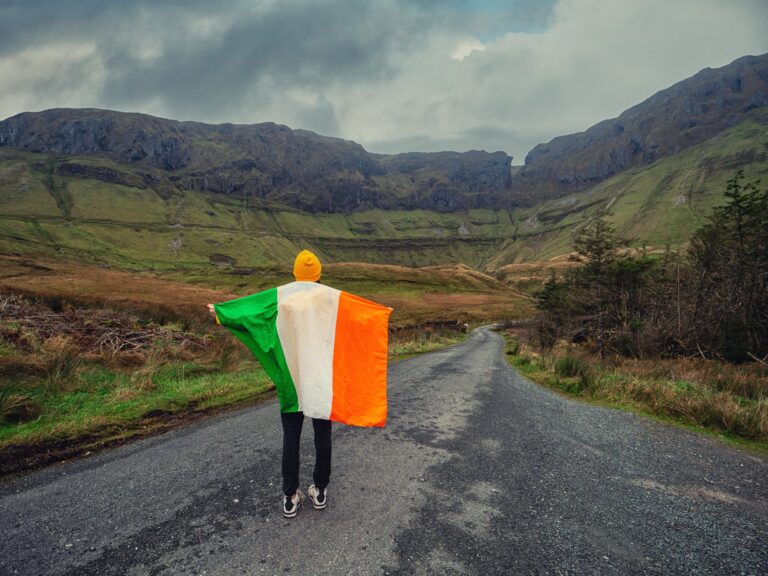 Foto av person som holder et stort, irsk flagg, i forgrunnen av irsk landskap.